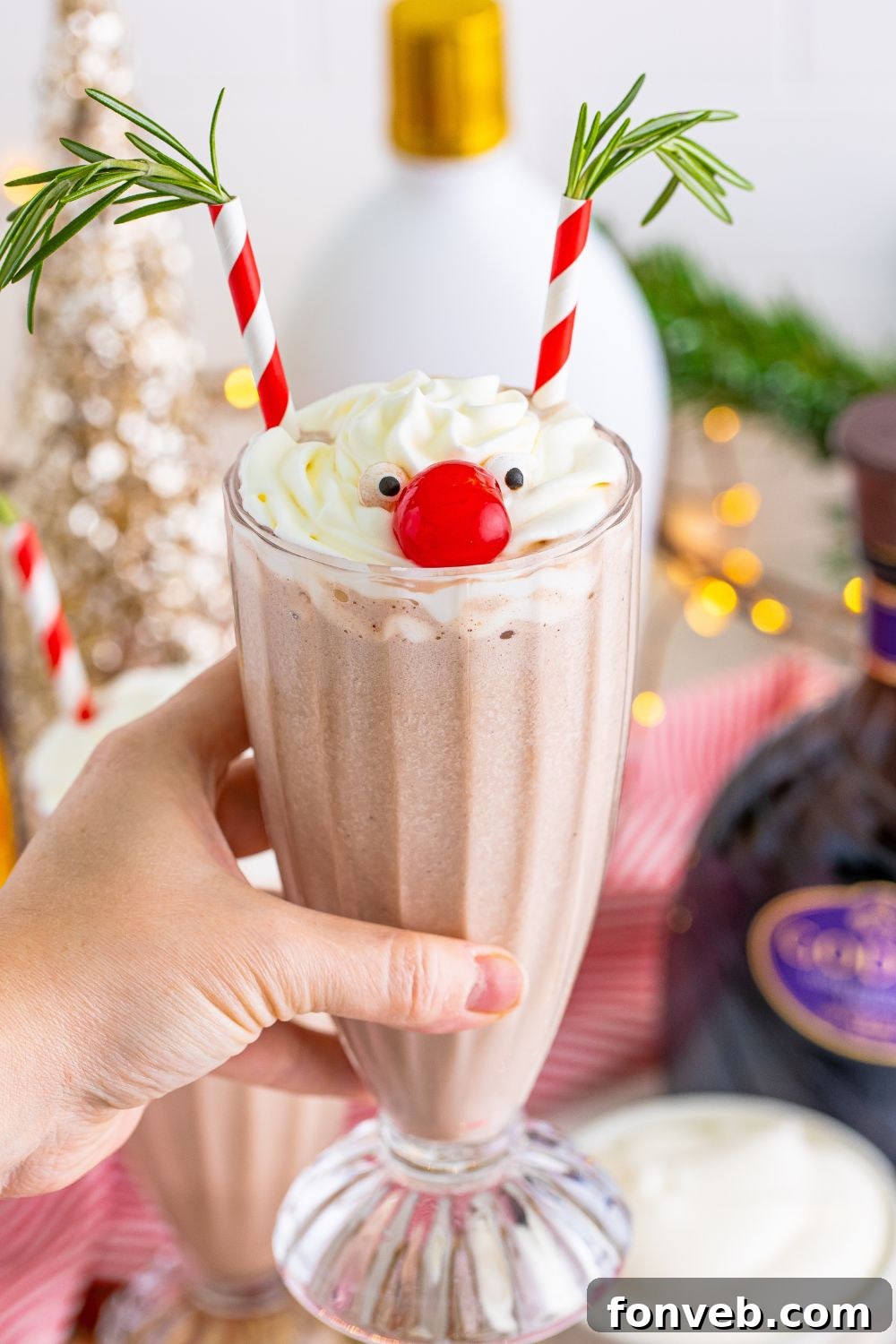A hand holding a Drunk Rudolph Milkshake above a festive table setting.
