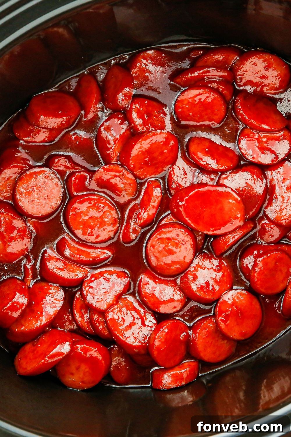Close-up of sliced sausage generously coated in the rich, glossy sauce in a slow cooker.
