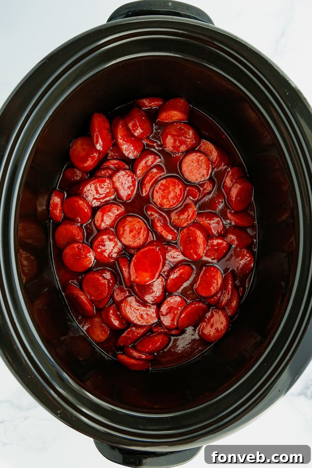 Overhead view of glistening kielbasa bites simmering in the slow cooker, perfectly coated in sauce.