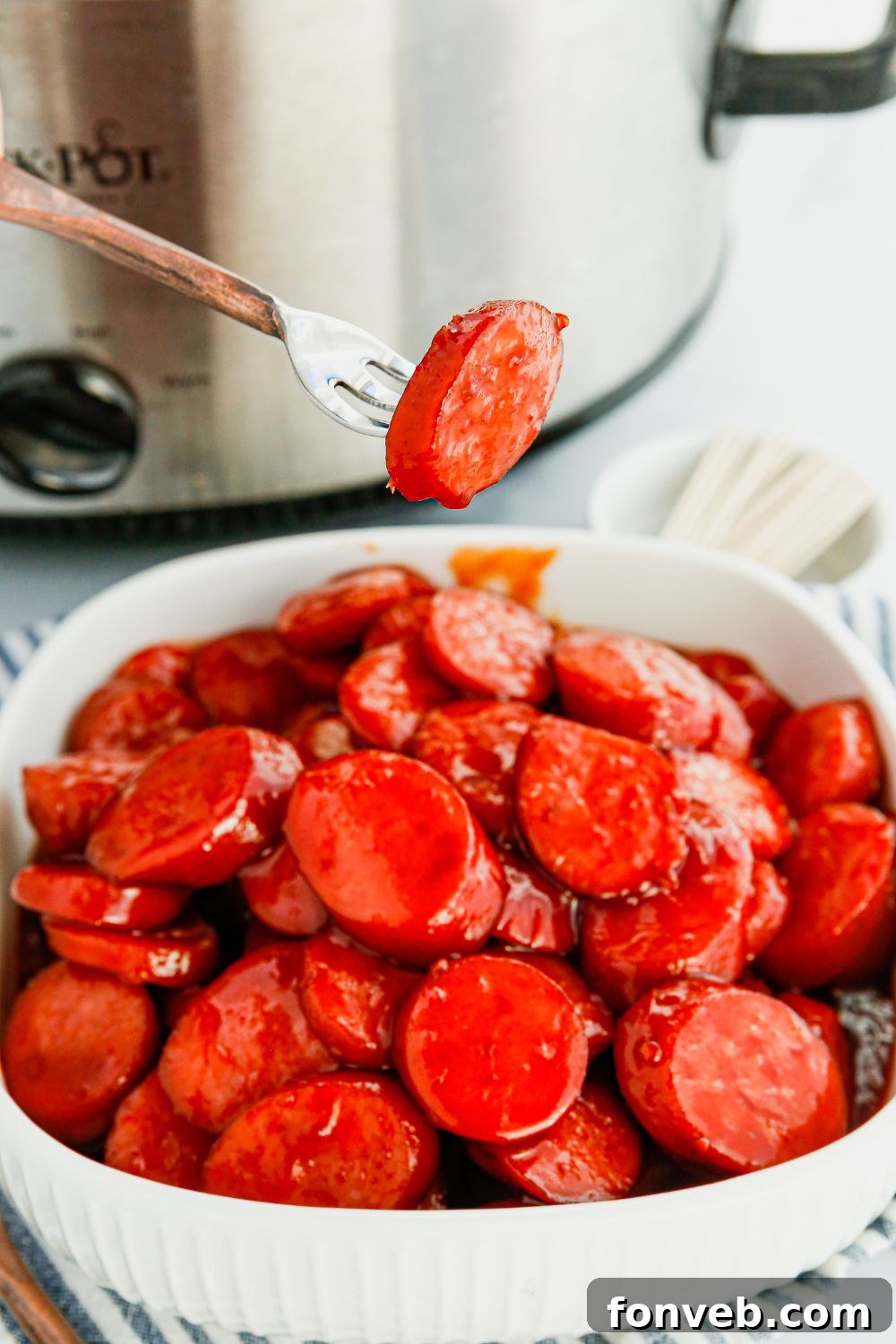 A single kielbasa bite perfectly balanced on a fork, showcasing its tender texture and glossy coating.