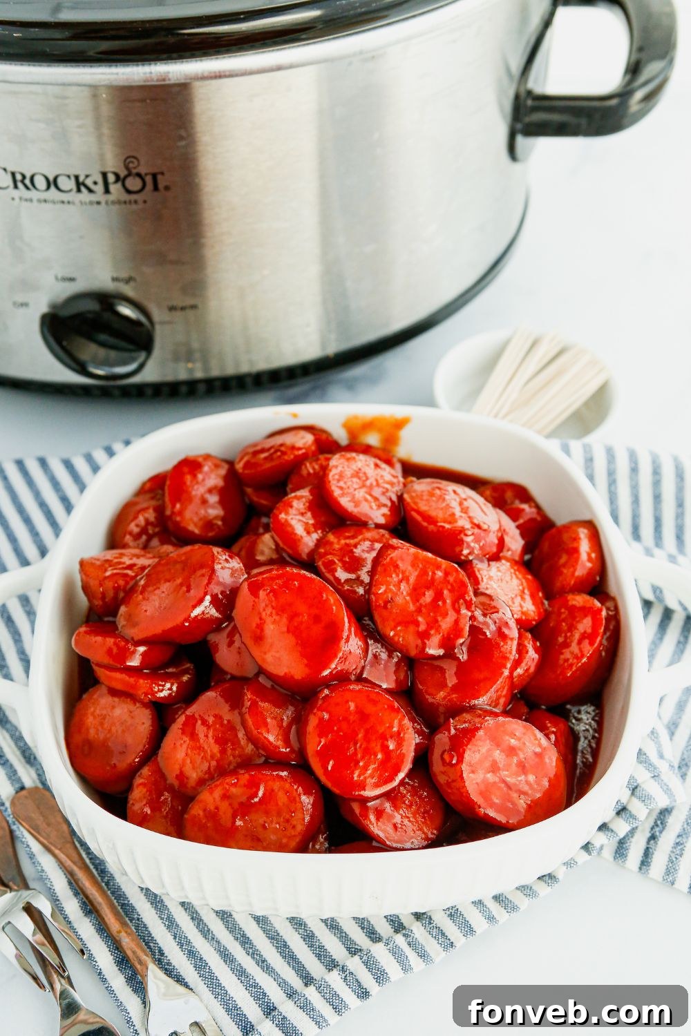 A serving bowl of kielbasa bites next to a slow cooker, ready for guests.