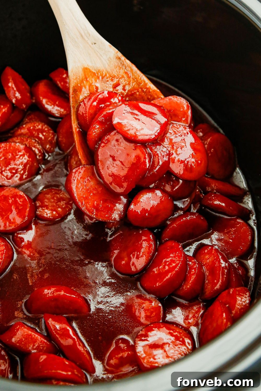Sliced kielbasa bites simmering in a sweet and spicy sauce inside a crockpot.