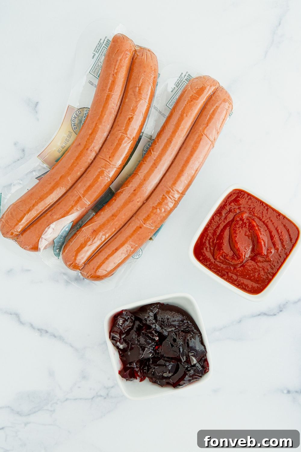 Ingredients for Crockpot Kielbasa Bites: kielbasa on a cutting board, with bowls of chili sauce and grape jelly.