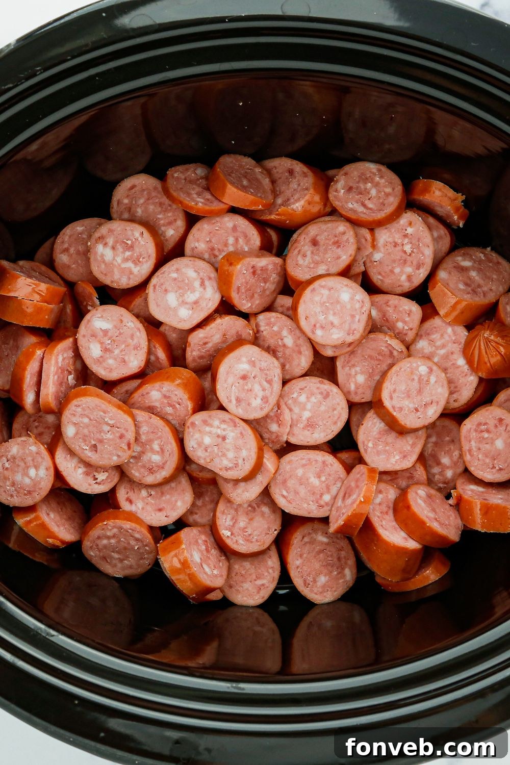 Sliced smoked sausage arranged neatly in a crockpot, ready for sauce.