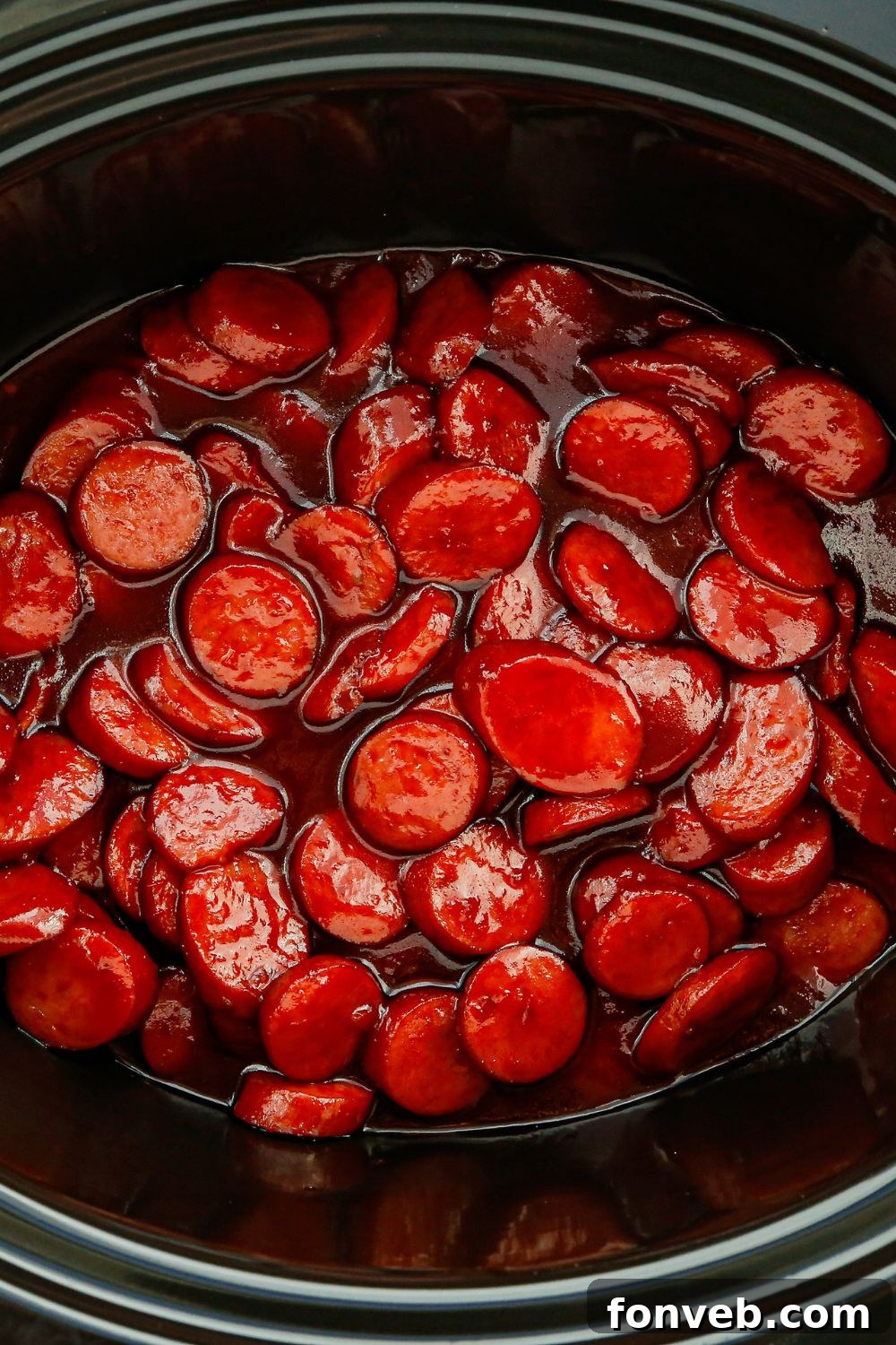 Kielbasa bites cooking in a slow cooker, simmering in a rich, glossy sauce.