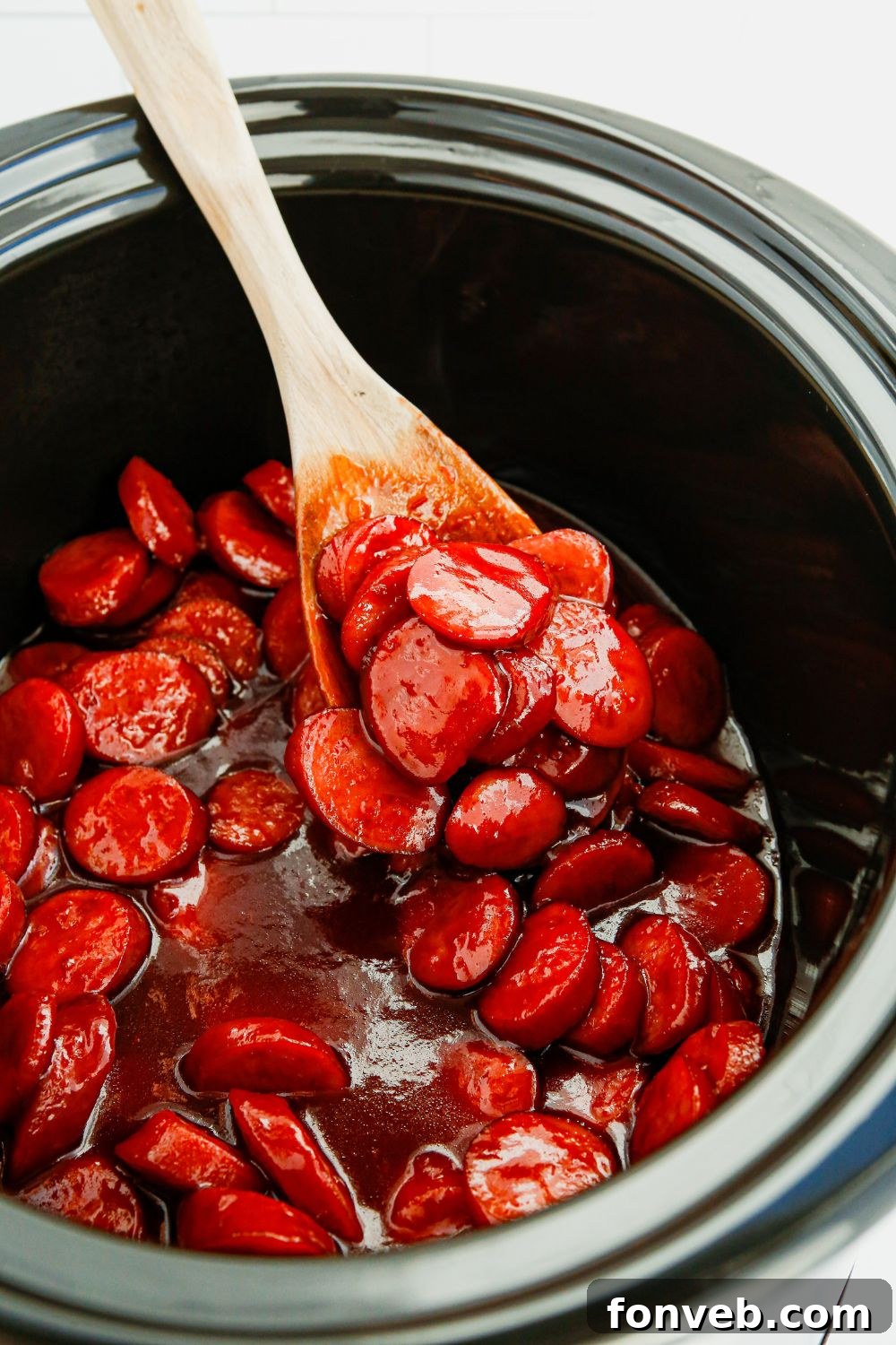 A single smoked sausage appetizer bite on a wooden spoon, showcasing its delicious glaze.