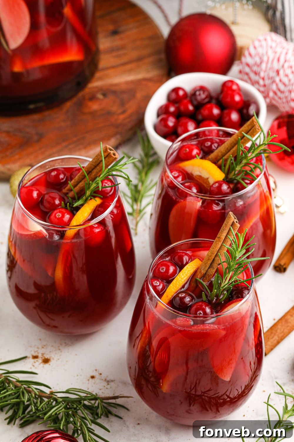 Glasses of Cranberry Apple Sangria adorned with cranberries, apple slices, and cinnamon sticks, set on a table with festive ornaments.