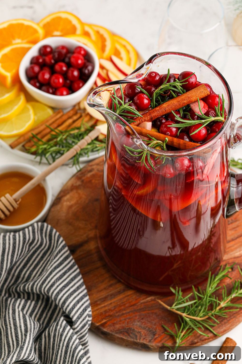 View of a pitcher filled with sangria, surrounded by fresh fruit and cinnamon sticks.