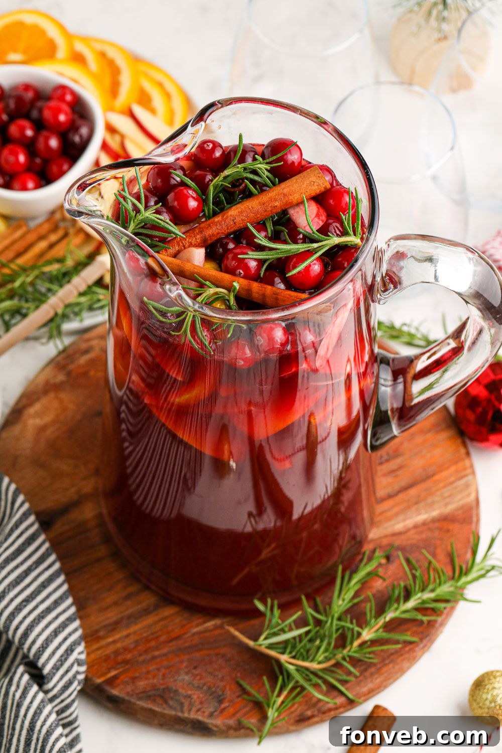 A pitcher of sangria garnished with cranberries, rosemary, and cinnamon sticks.