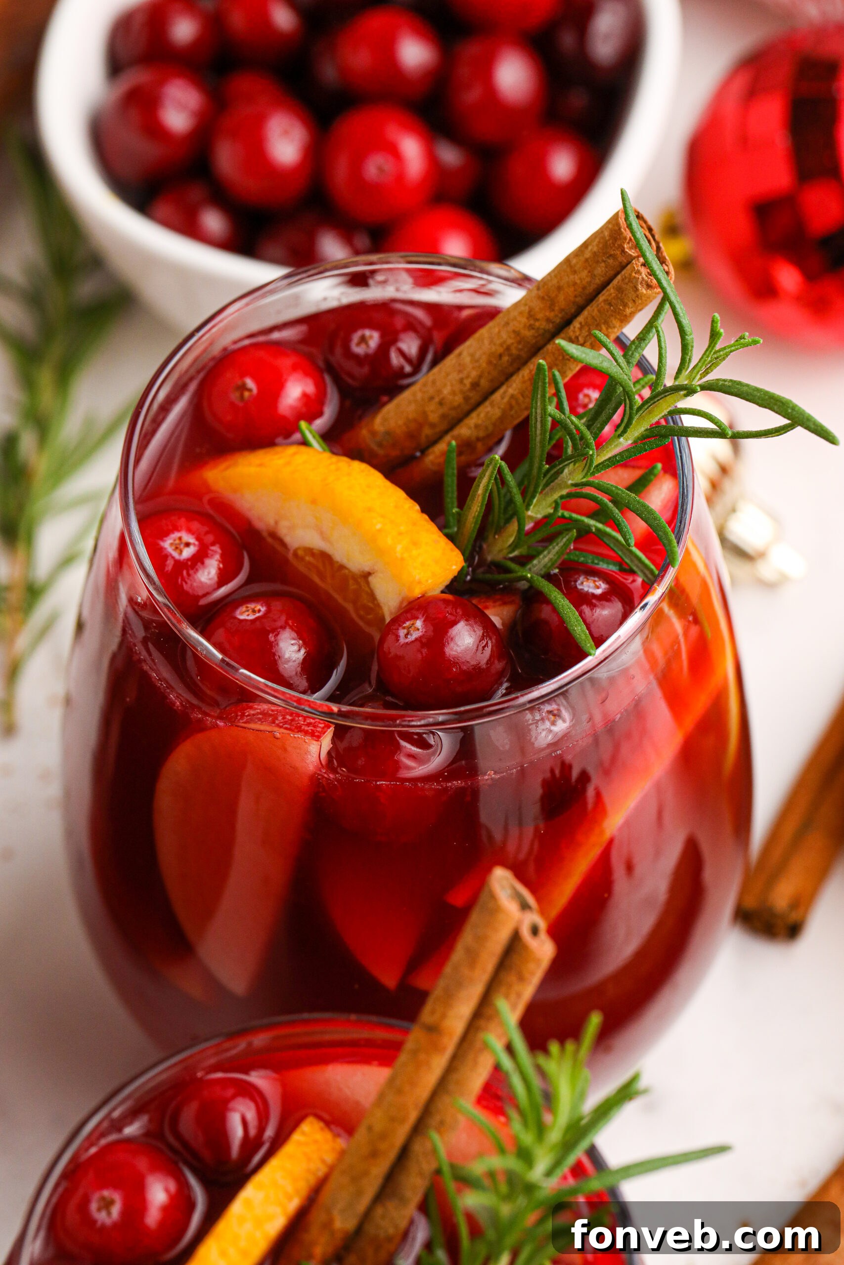 Cranberry Apple Christmas Sangria in a clear glass, with fresh cranberries, apple slices, and cinnamon sticks.