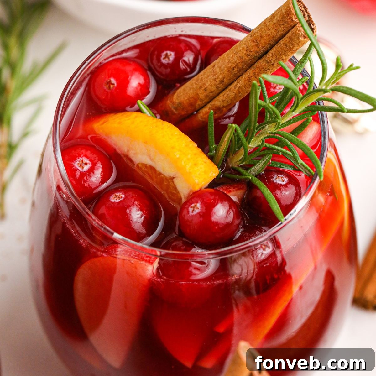 Close-up of Cranberry Apple Christmas Sangria in a glass, showcasing fresh cranberries, apple slices, and a rosemary sprig garnish.