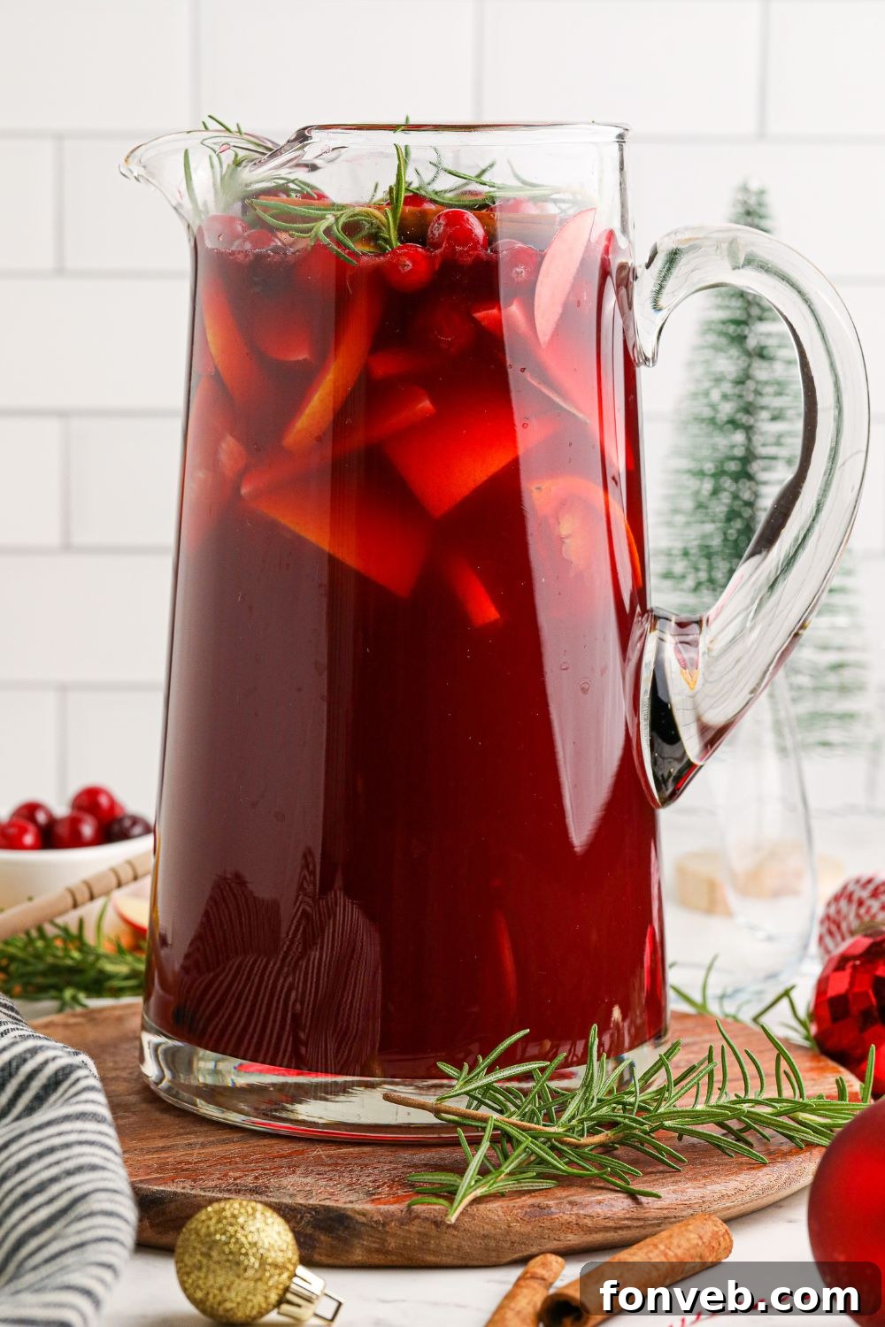 A glass pitcher filled with Cranberry Apple Christmas Sangria, garnished with fruit and rosemary, ready to be served.