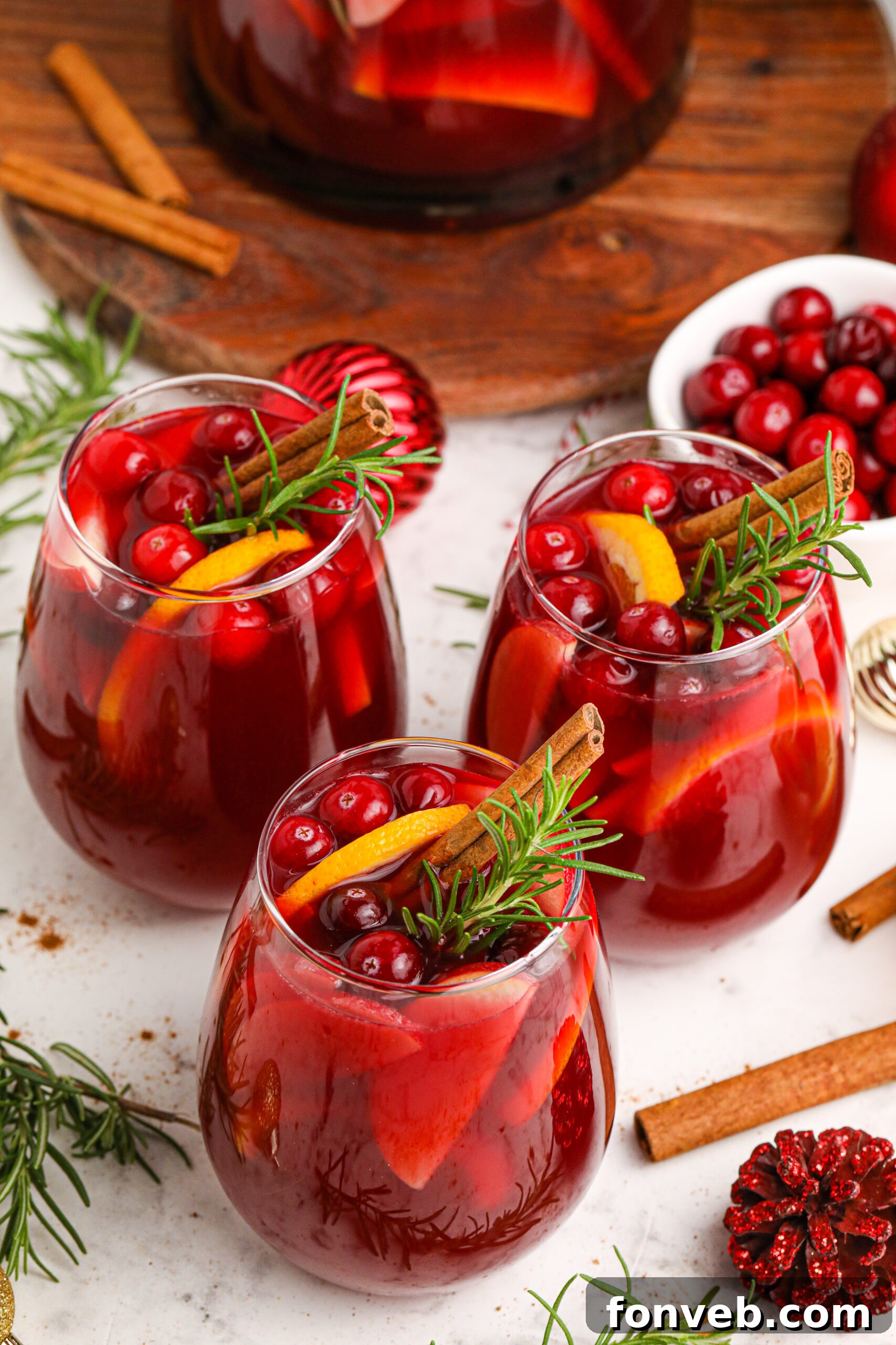 Three glasses of Cranberry Apple Christmas Sangria, garnished with fresh cranberries, apple slices, and cinnamon sticks.