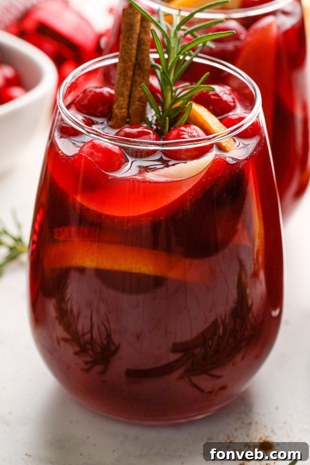Side view of a glass of sangria with fruit and ice on a marble table.