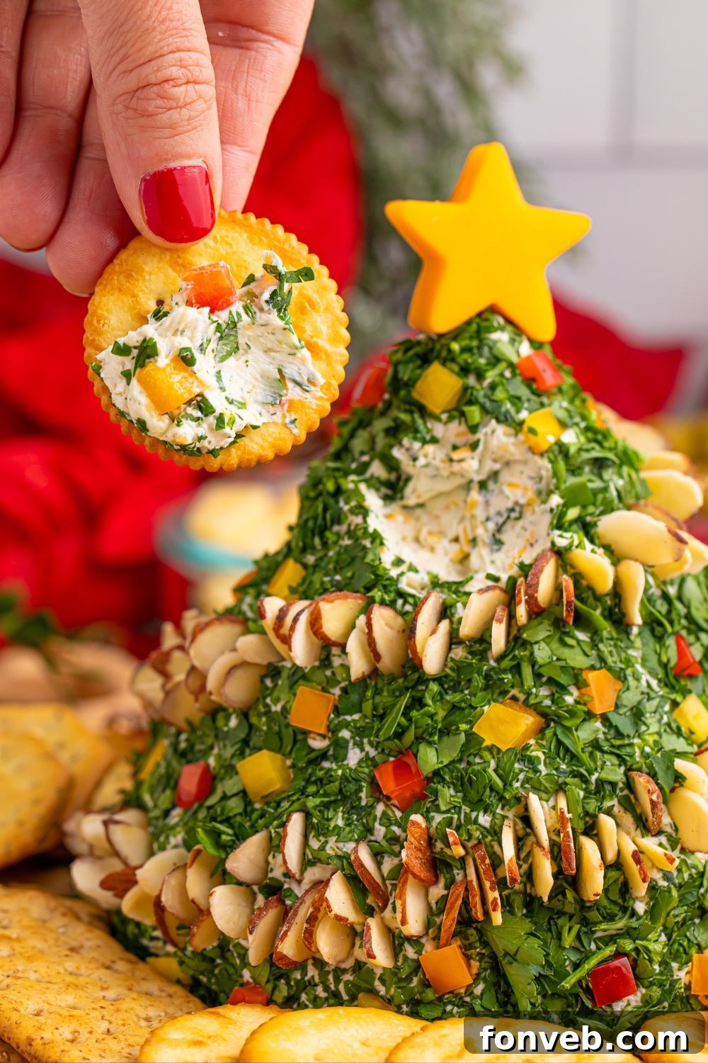 A hand holding a cracker with a generous spread of Christmas Tree Cheeseball