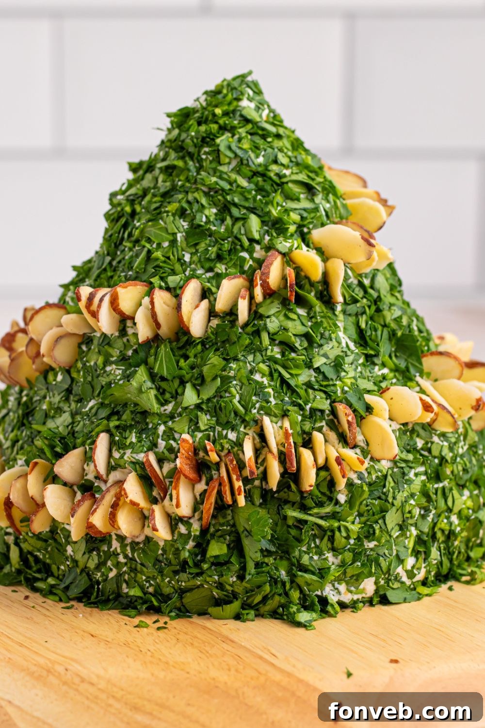 Side view of the cheeseball being decorated with slivered almonds and bell peppers