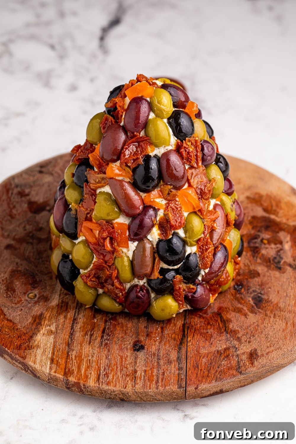 Olives and dried tomatoes pressed onto the outside of a cheeseball tree