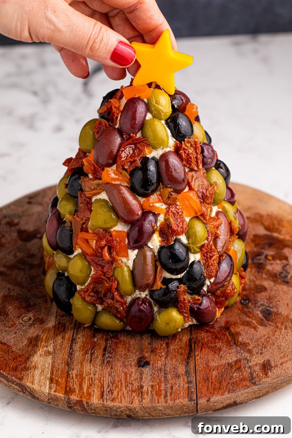 Cheeseball decorated with olives and a cheese star being placed on top with a toothpick