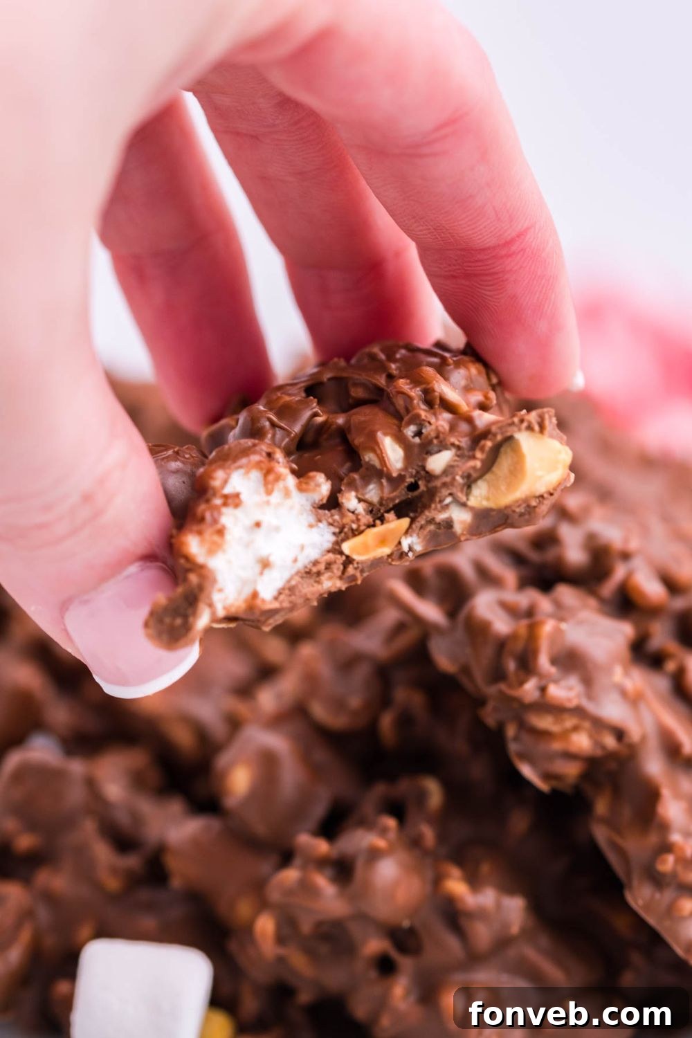 A person holding a piece of Rocky Road Candy with a bite taken, showing the rich interior.