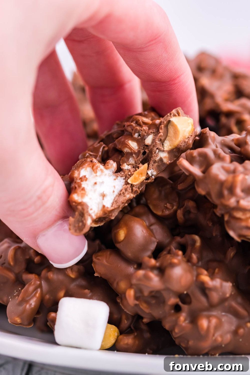 A hand holding a piece of Rocky Road Candy with a bite taken out, showing the sweet interior.