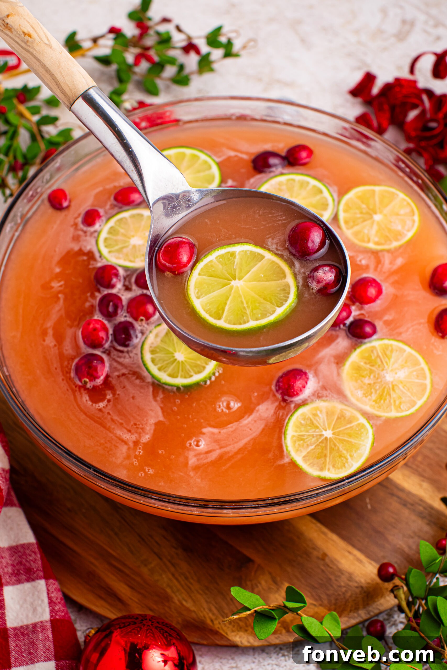 Large punch bowl filled with Santa's Giggle Juice Punch, garnished with cranberries and lime slices, with a serving spoon poised to fill a cup.