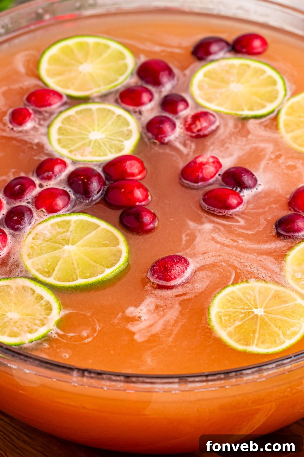 Santa's Giggle Juice Punch in a large bowl, garnished with cranberries and lime, with a ladle ready to serve, set against a festive backdrop.