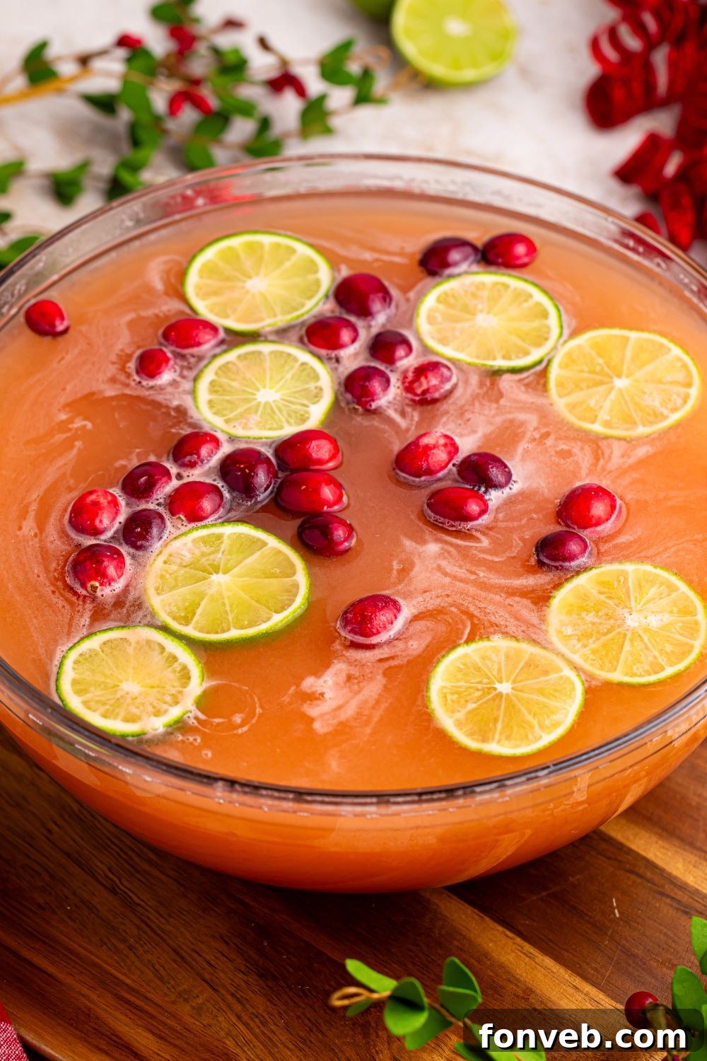 A large bowl of vibrant Christmas cocktail punch, garnished with fresh fruit, set to be served at a holiday event.