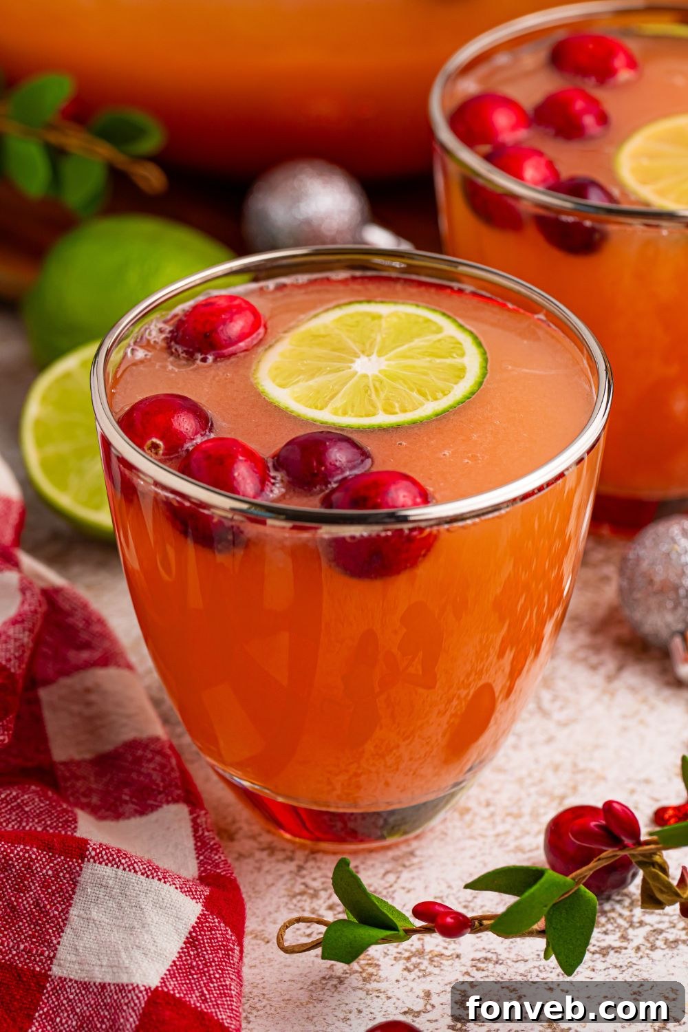 Individual glasses of Santa's Giggle Juice Punch, beautifully garnished with fresh cranberries and lime wedges, sitting on a wooden table.
