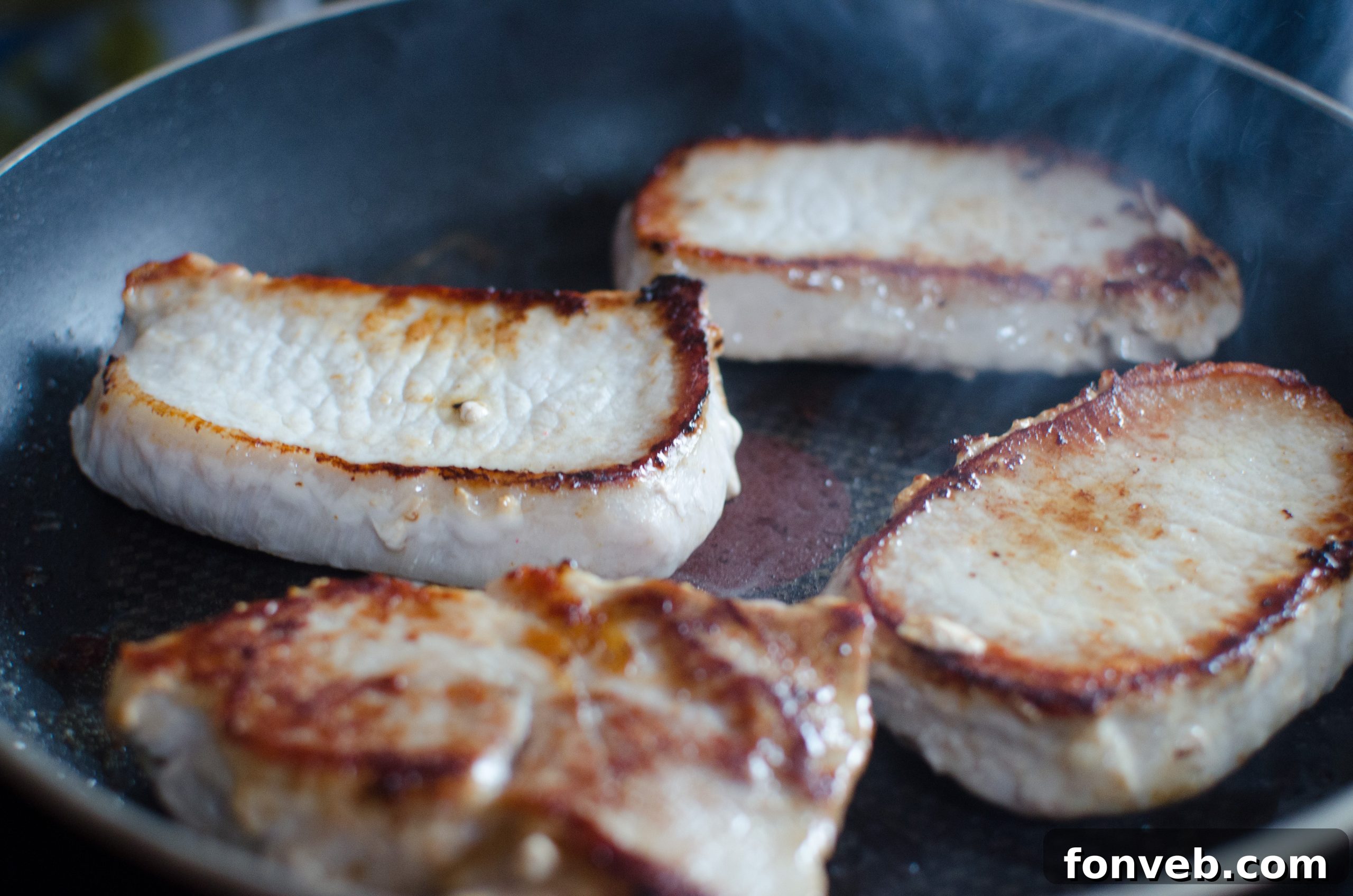 Raw boneless pork chops seasoned generously with a mix of spices, ready for searing.