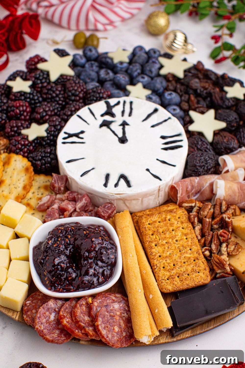A festive New Year's Eve Charcuterie Board displayed on a table, adorned with elegant Christmas decorations, featuring a round board brimming with delectable snacks.