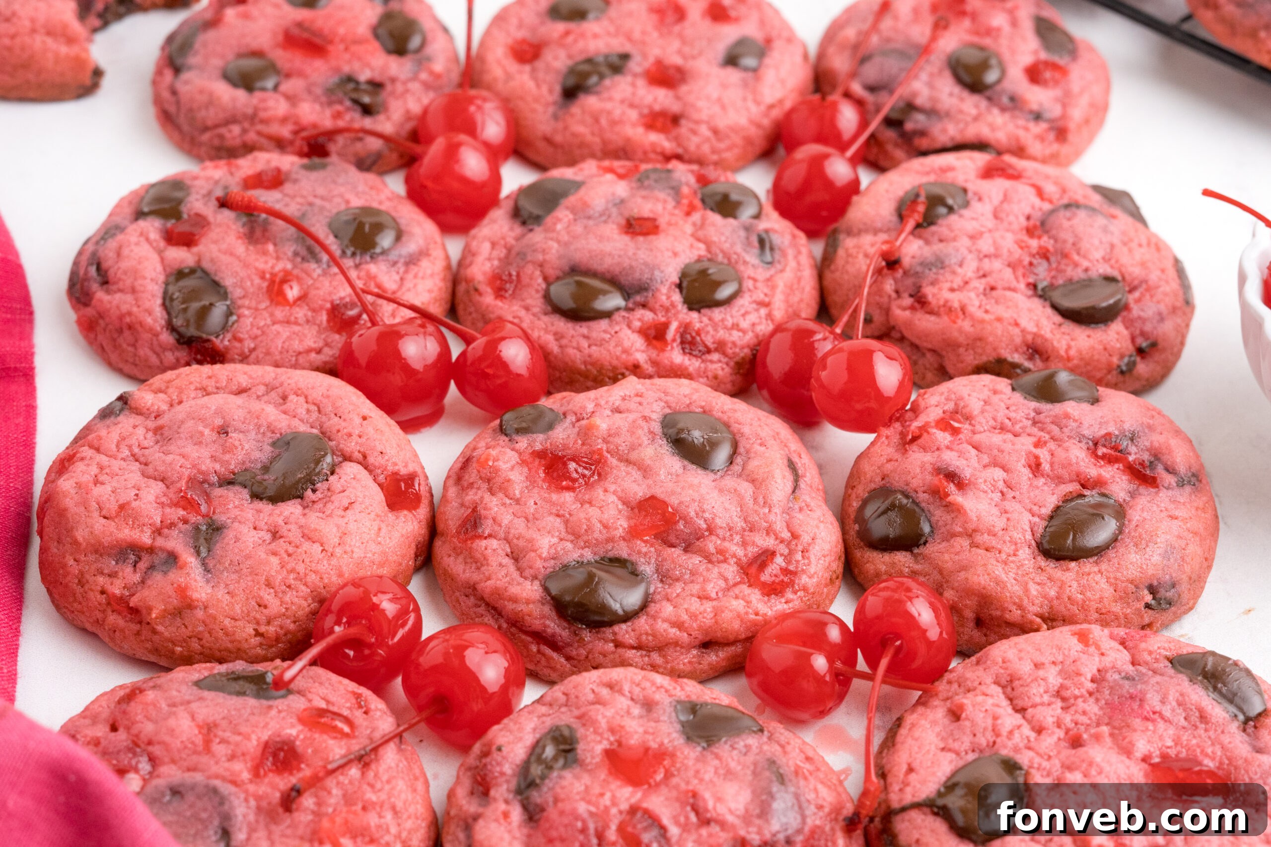Cherry Chocolate Chip Cookies placed on table with maraschino cherries in between cookies on table to offer color and cookies in a single line 