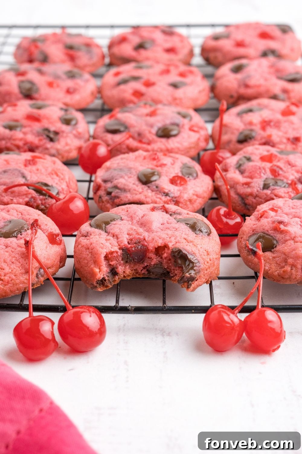 Cherry Chocolate Chip Cookies placed on a cooling rack, with one cookie in the center of tray with a bite taken out of it 