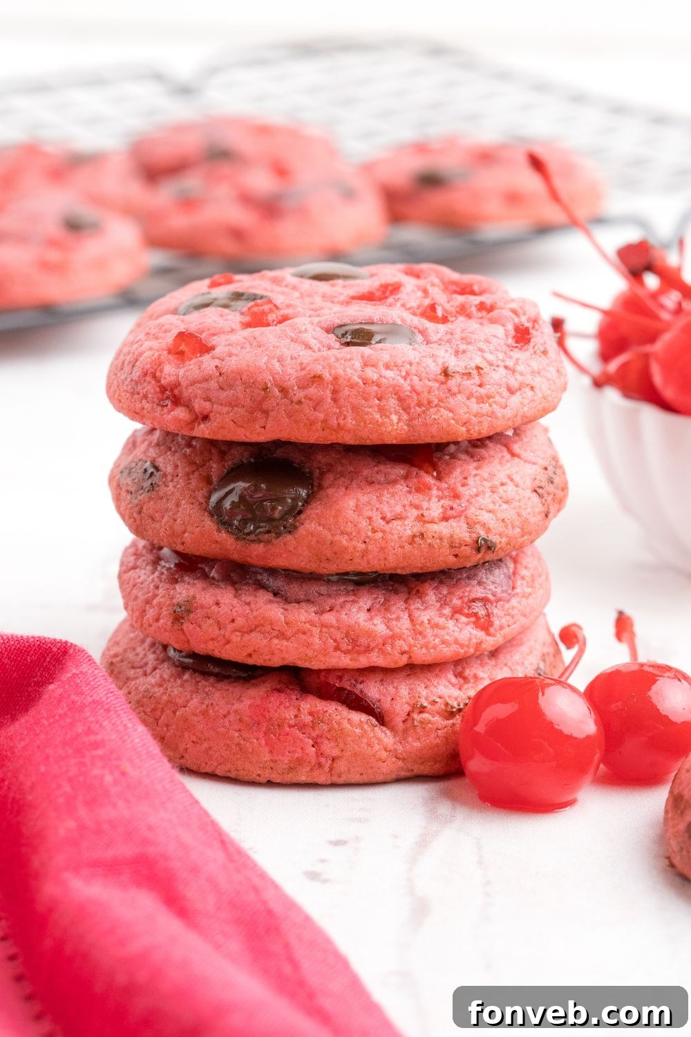 stacked Cherry Chocolate Chip Cookies on the table with two cherries sitting by it 