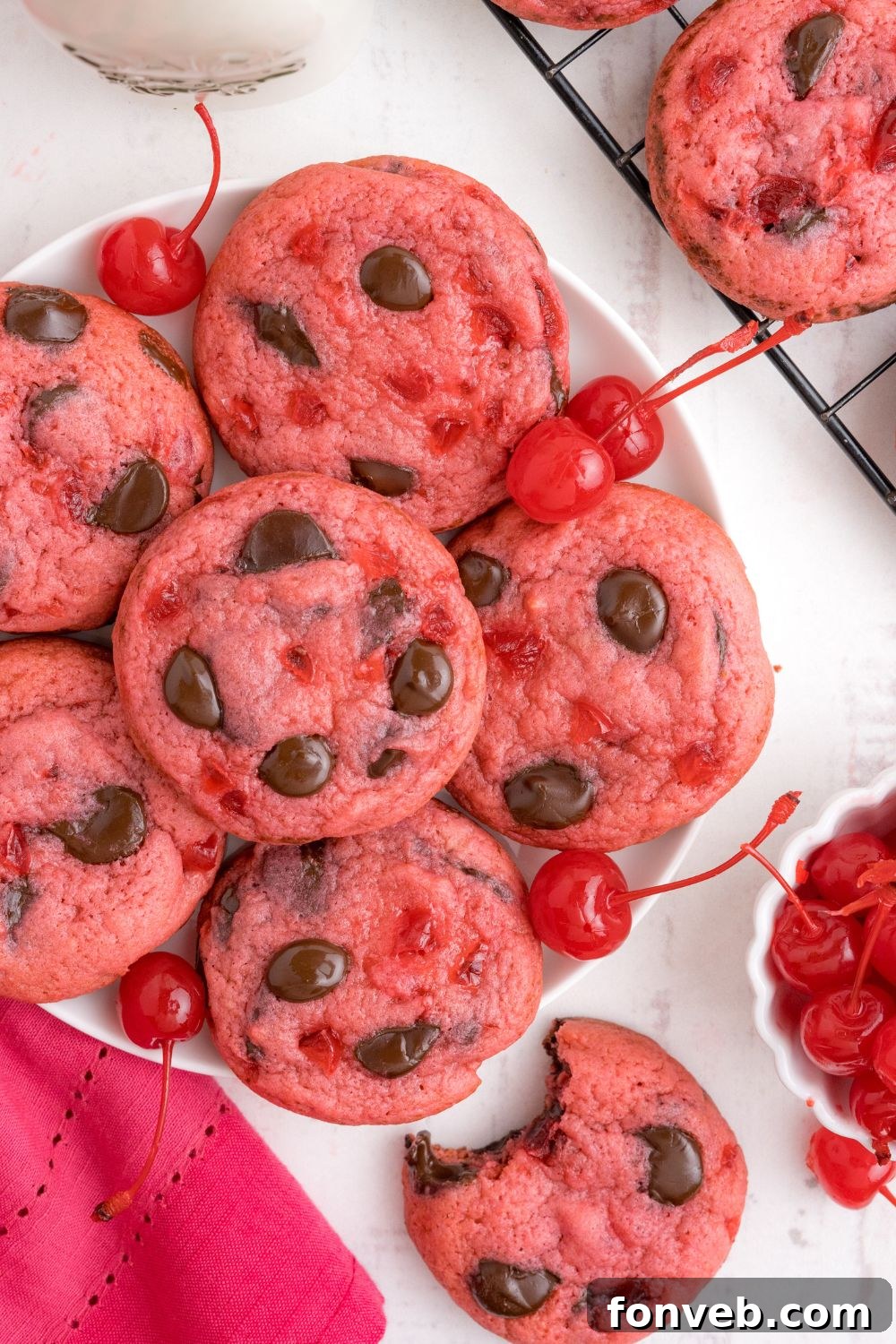 Cherry Chocolate Chip Cookies on a plate with one cookie with a bite taken out placed on table and a bowl of cherries on side 