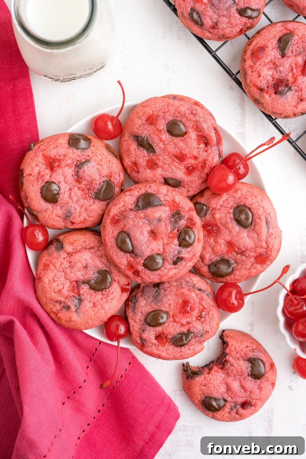 Cherry Chocolate Chip Cookies on a plate with a glass of milk and a bite of cookie taken out of one cookie 