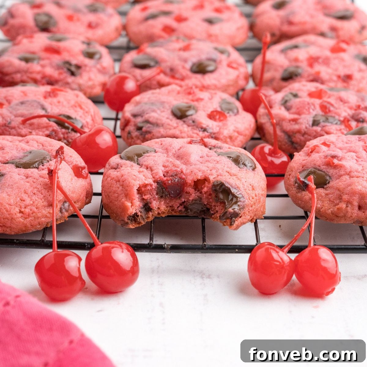 Cherry Chocolate Chip Cookies on a cookie tray with a few cherries on the table in front of the container 