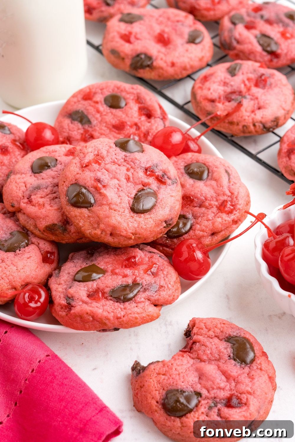 Cherry Chocolate Chip Cookies side view with a plate stacked of cookies and a tall glass of milk beind the plate 