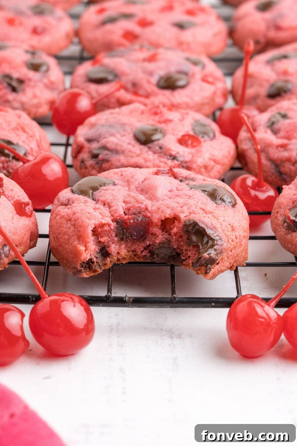 close up of cookies on a metal cooling rack with a few maraschino cherries scattered on the table 