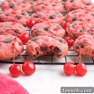 Cherry Chocolate Chip Cookies on a cookie tray with a few cherries on the table in front of the container