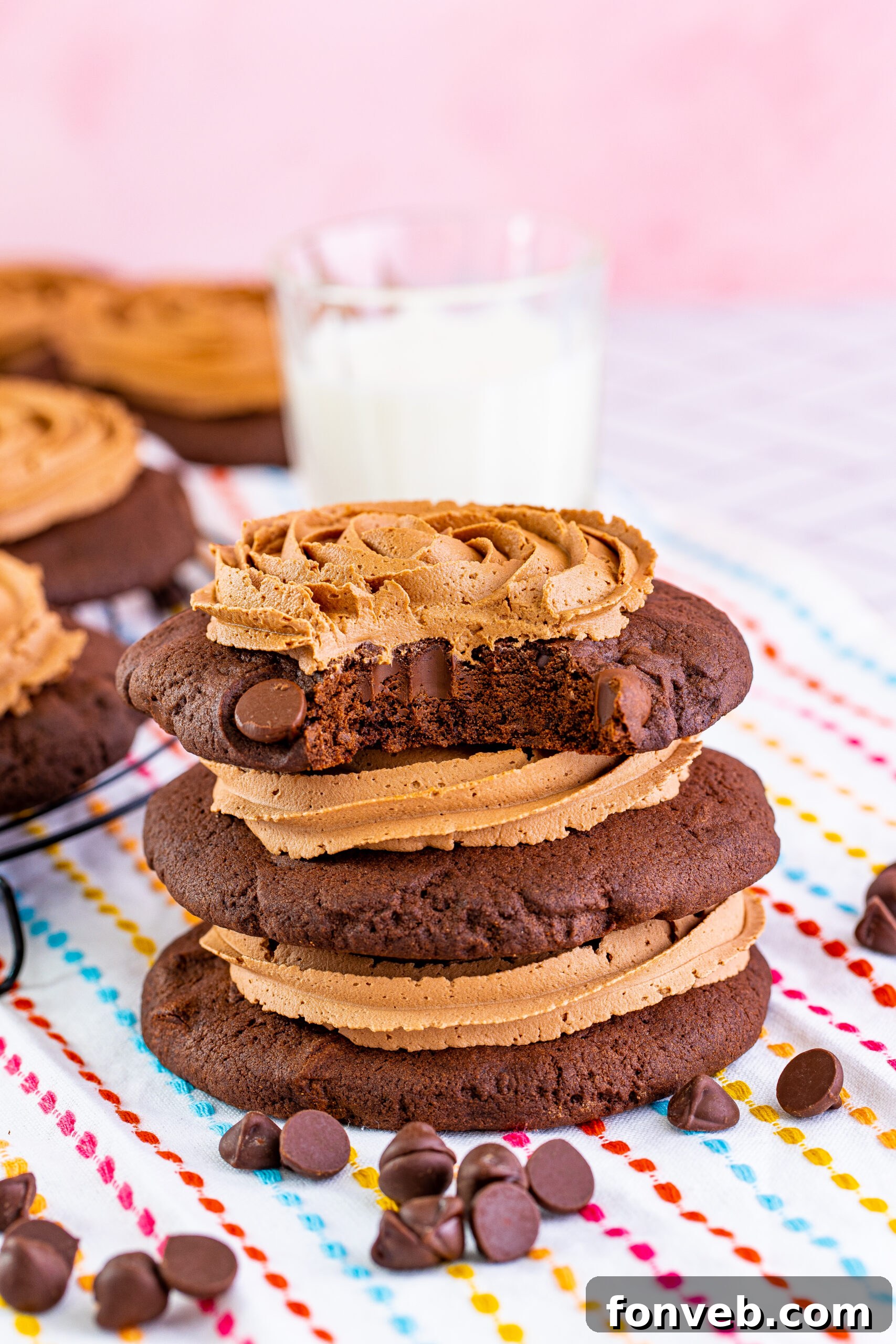 Stacked Chocolate Cake Cookies with rich chocolate fudge frosting and a bite taken from the top cookie, showcasing its soft interior