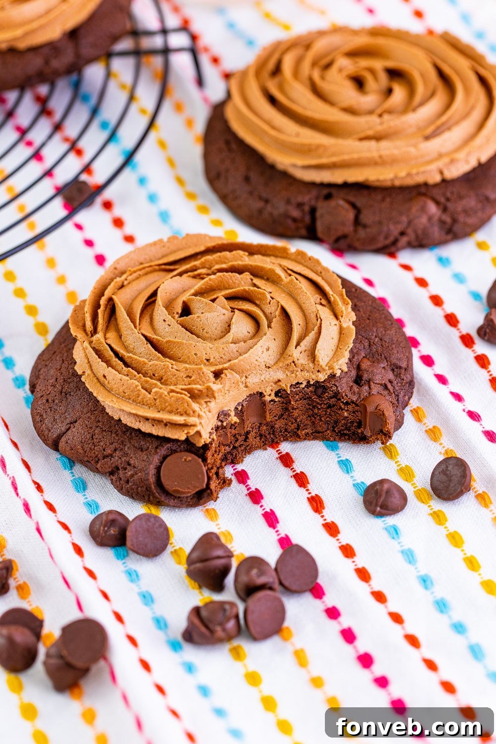 A close-up of a Chocolate Cake Cookie with a bite taken out, resting on a table with mini chocolate chips scattered around it