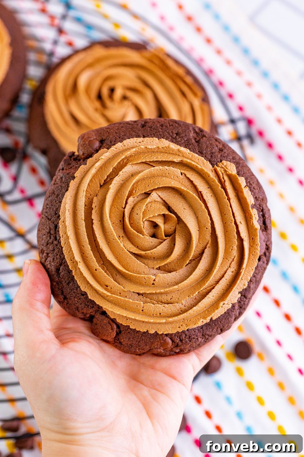 A hand holding a perfectly frosted Chocolate Cake Cookie, ready to be enjoyed