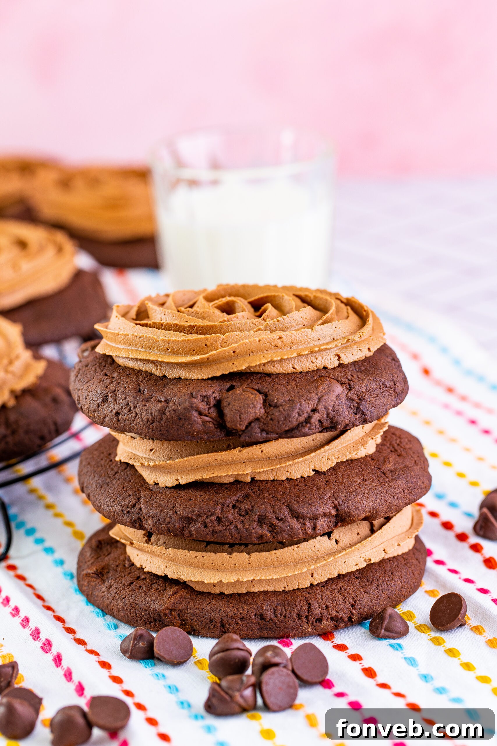 A stack of beautifully frosted Chocolate Cake Cookies with a glass of milk in the background, a classic pairing