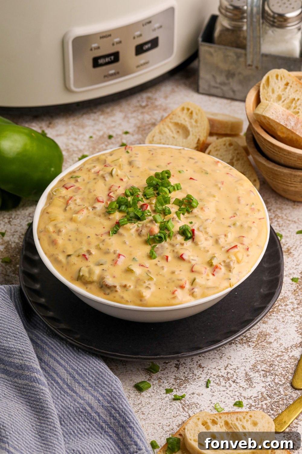 Crock Pot Philly Cheesesteak Dip in a white bowl on table with peppers around it on counter and bread slices