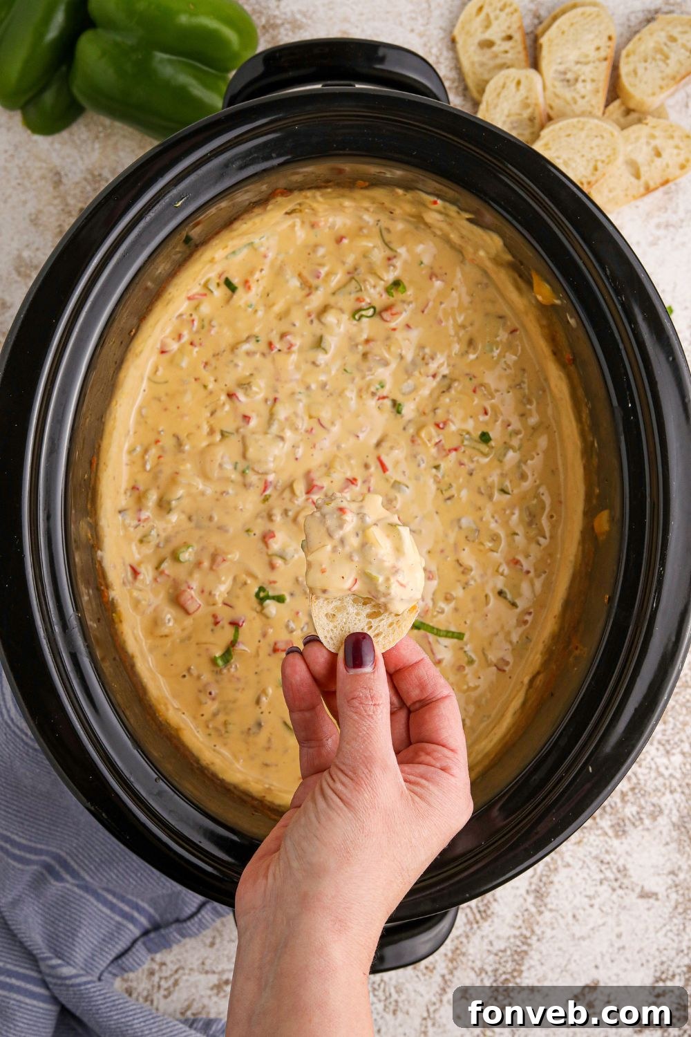 Crock Pot Philly Cheesesteak Dip with a hand and a piece of bread dipped in the creamy dip above the crockpot