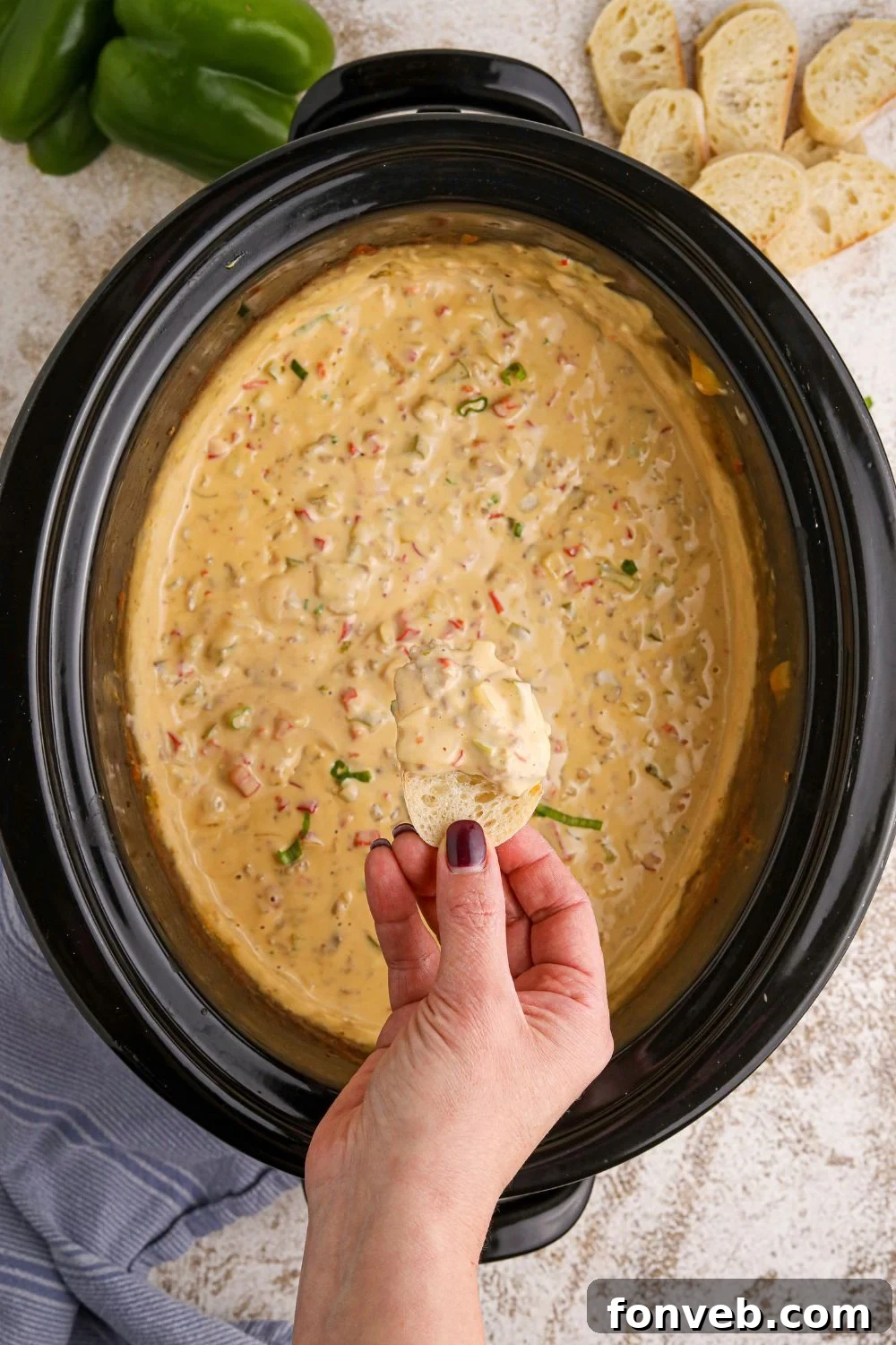 Crock Pot Philly Cheesesteak Dip with a hand and a piece of bread dipped in the creamy dip above the crockpot