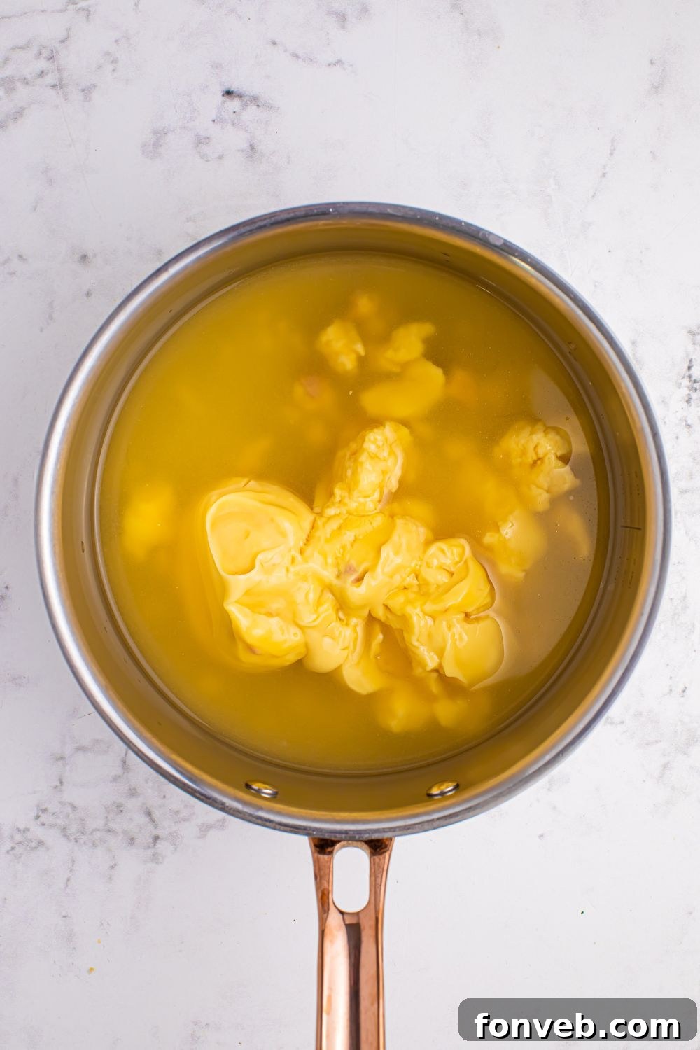 Chicken stock and condensed soup being whisked together in a saucepan.