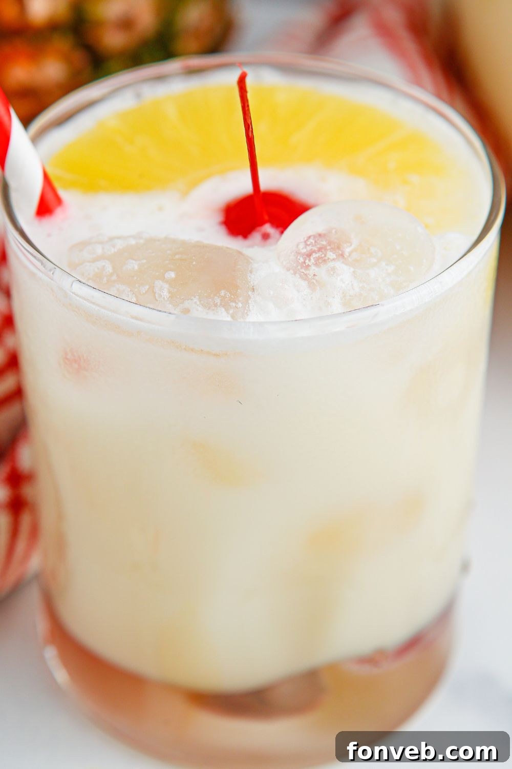 Island Escape Punch 12 A glass of Piña Colada Punch with a cherry in the center, sitting on a wooden table.