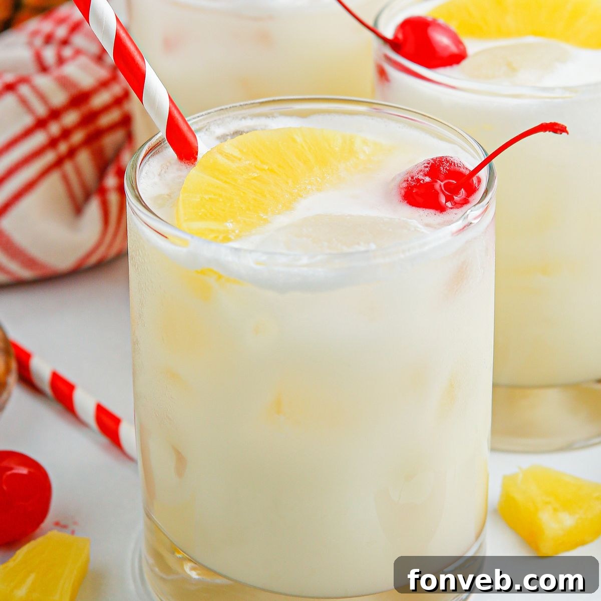 Island Escape Punch 3 Clear glasses filled with frothy Piña Colada Punch, each with a festive red and white striped straw and a cherry garnish.