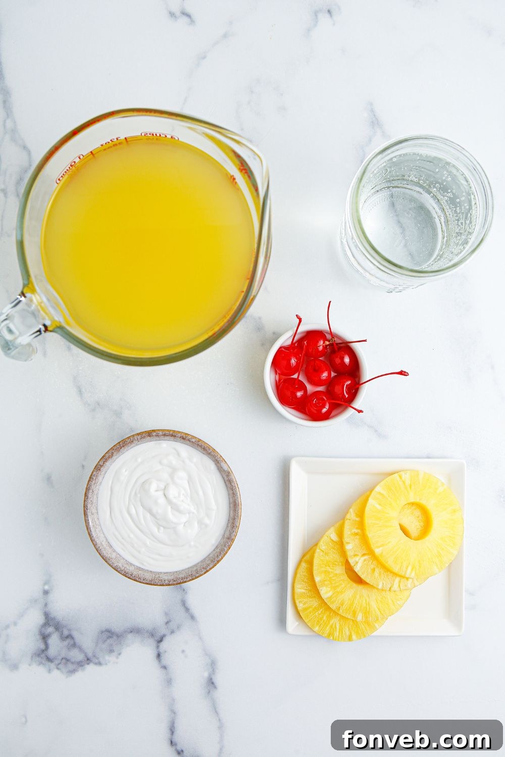 Island Escape Punch 5 All the ingredients for Piña Colada Punch laid out on a table: a pitcher of pineapple juice, a can of cream of coconut, sparkling water, a bowl of fresh cherries, and pineapple wedges.